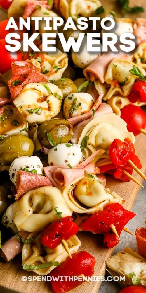 an assortment of skewers on a wooden board with tomatoes and other food items