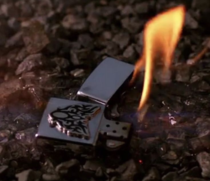 a lighter that is on some rocks with fire coming out of the top and bottom