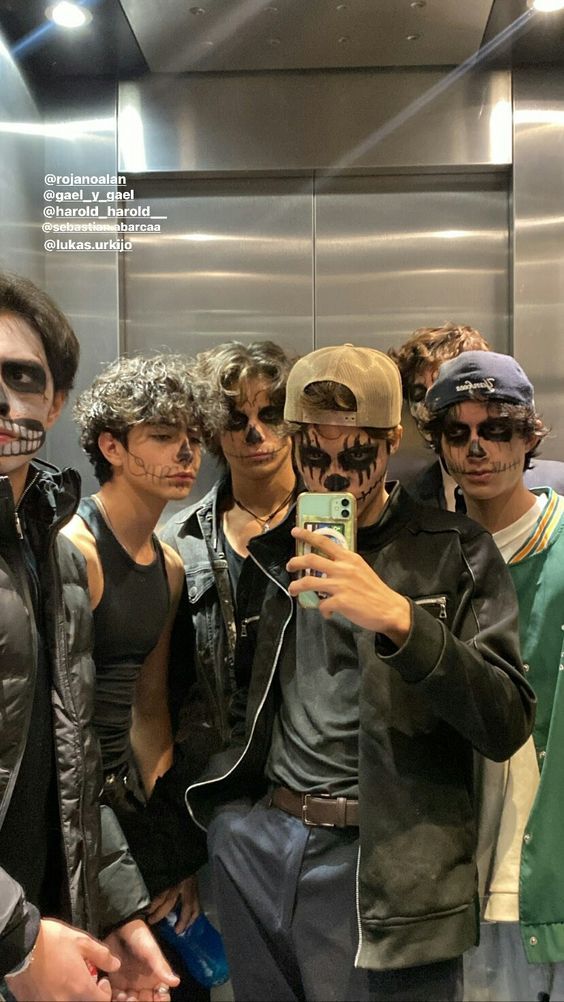 a group of young men standing next to each other in front of a mirror with their faces painted