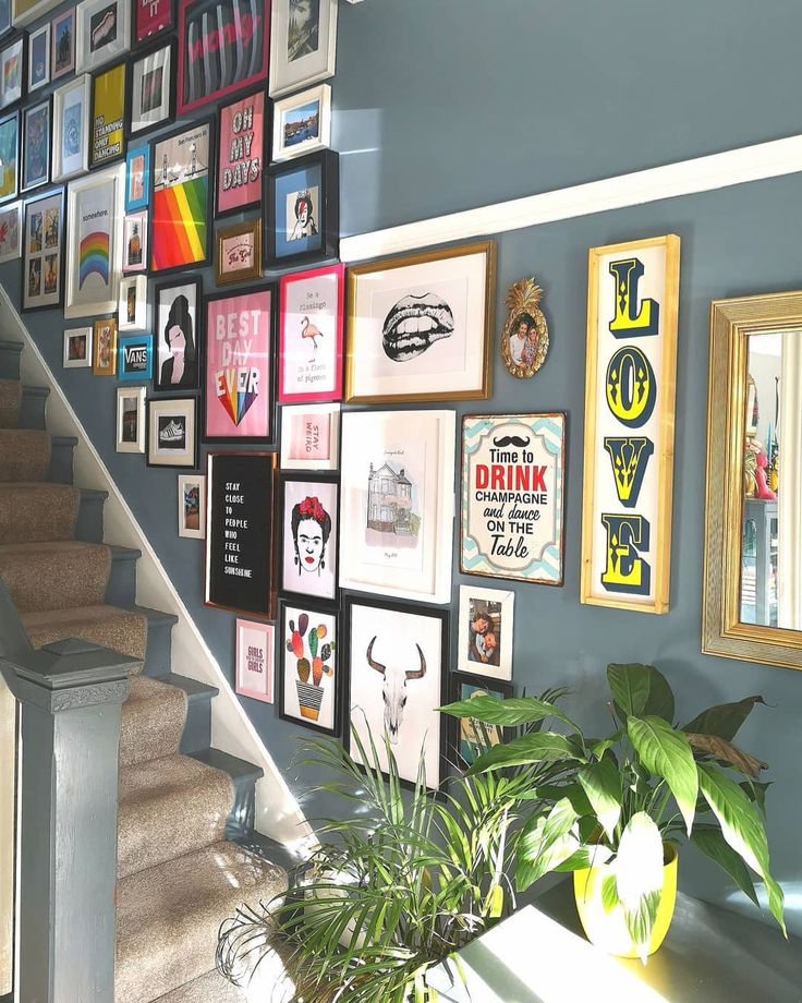 there is a staircase with many pictures on the wall next to it and a potted plant