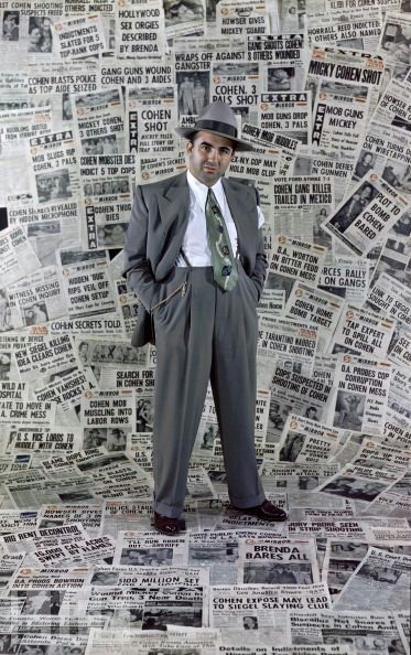 a man in a suit and tie standing on top of a pile of newspapers with his hands behind his back