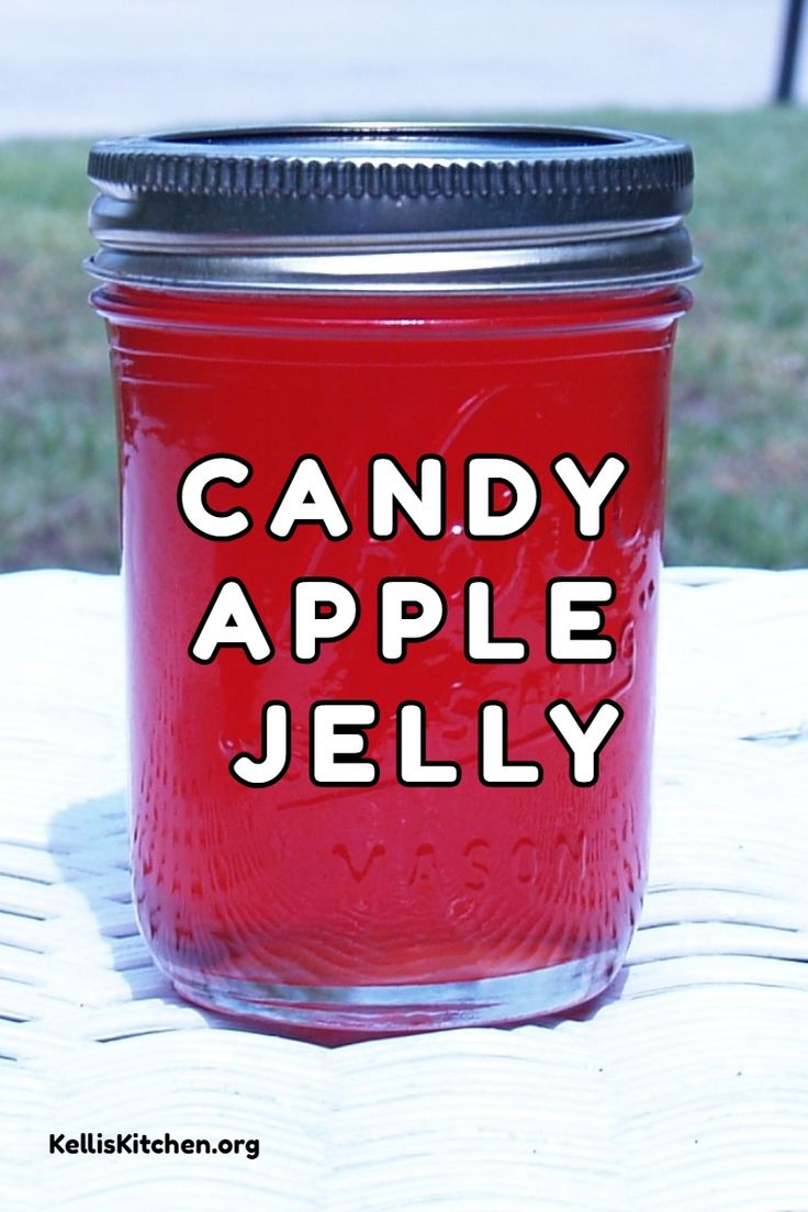 a red jar with candy apple jelly in it sitting on a white table outside next to some grass