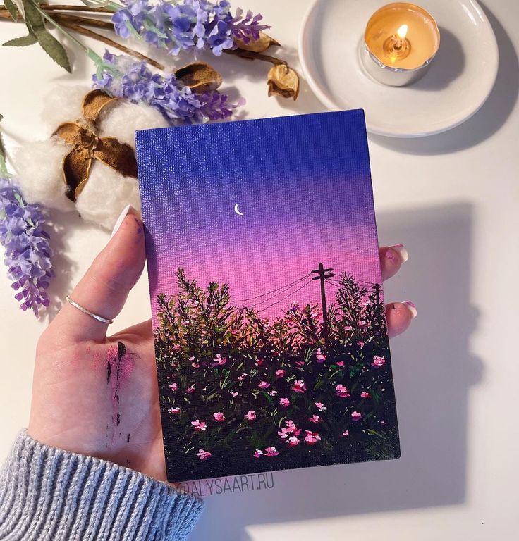 a person holding up a card with flowers on it and a candle in the background