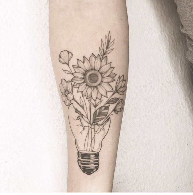 a sunflower in a lightbulb tattoo on the arm