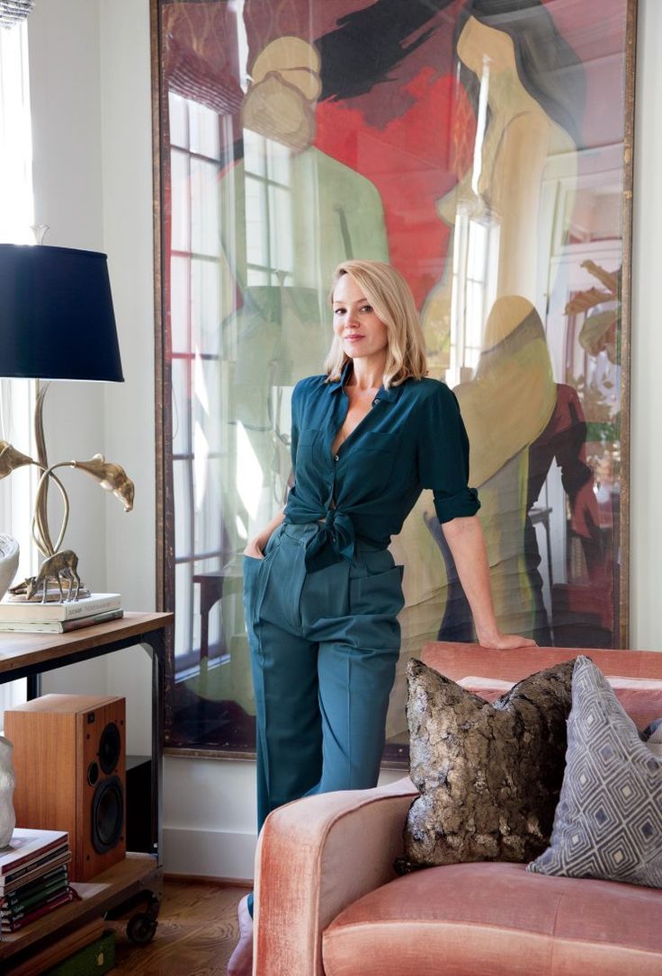 a woman standing next to a couch in front of a large painting on the wall