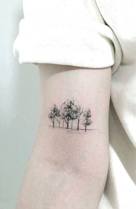 a small tree tattoo on the right inner arm, with three trees in the background