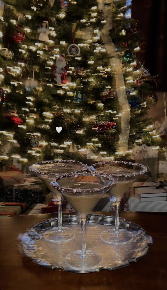 two martini glasses sitting on top of a table next to a christmas tree with lights