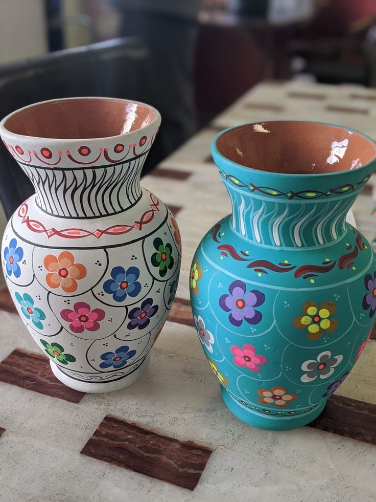 two colorful vases sitting on top of a table next to each other, one with flowers painted on it