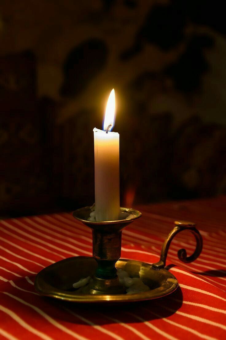 a lit candle sitting on top of a golden plate with a red and white table cloth