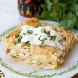 a white plate topped with lasagna covered in sour cream and garnished with cilantro