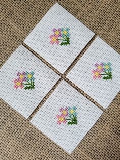 four cross stitch coasters with flowers on them sitting on a cloth covered tablecloth