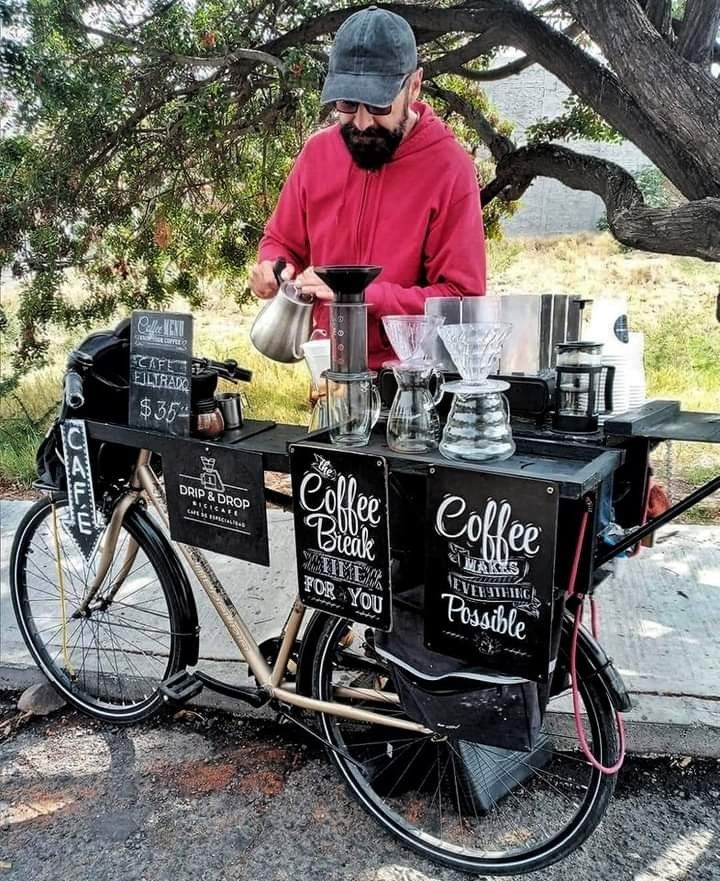 a man standing next to a bike with coffee on the front and side tables behind it