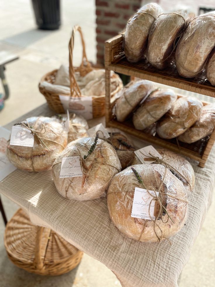 breads and pastries are on display at the market table in front of a brick building