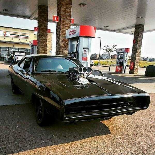 a black muscle car parked in front of a gas station