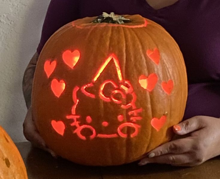 a woman holding a carved pumpkin with hearts on it