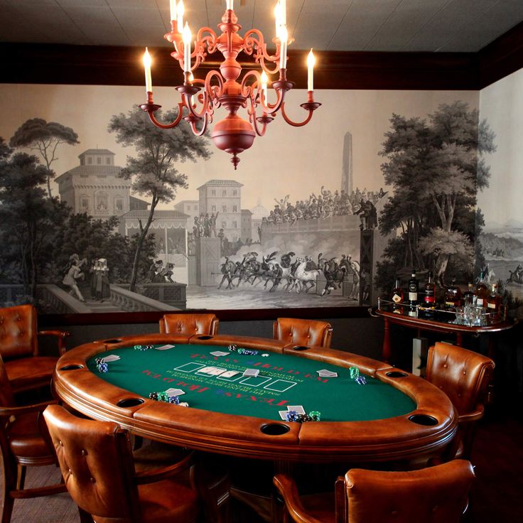 a casino table in front of a wall with a painting on it and chandelier hanging from the ceiling