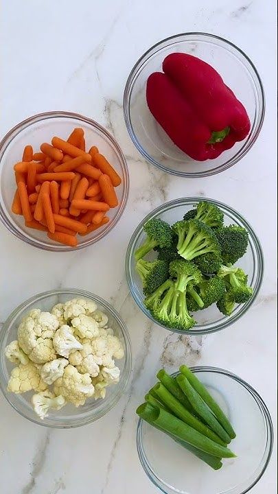 four bowls filled with different types of vegetables on top of a white marble countertop