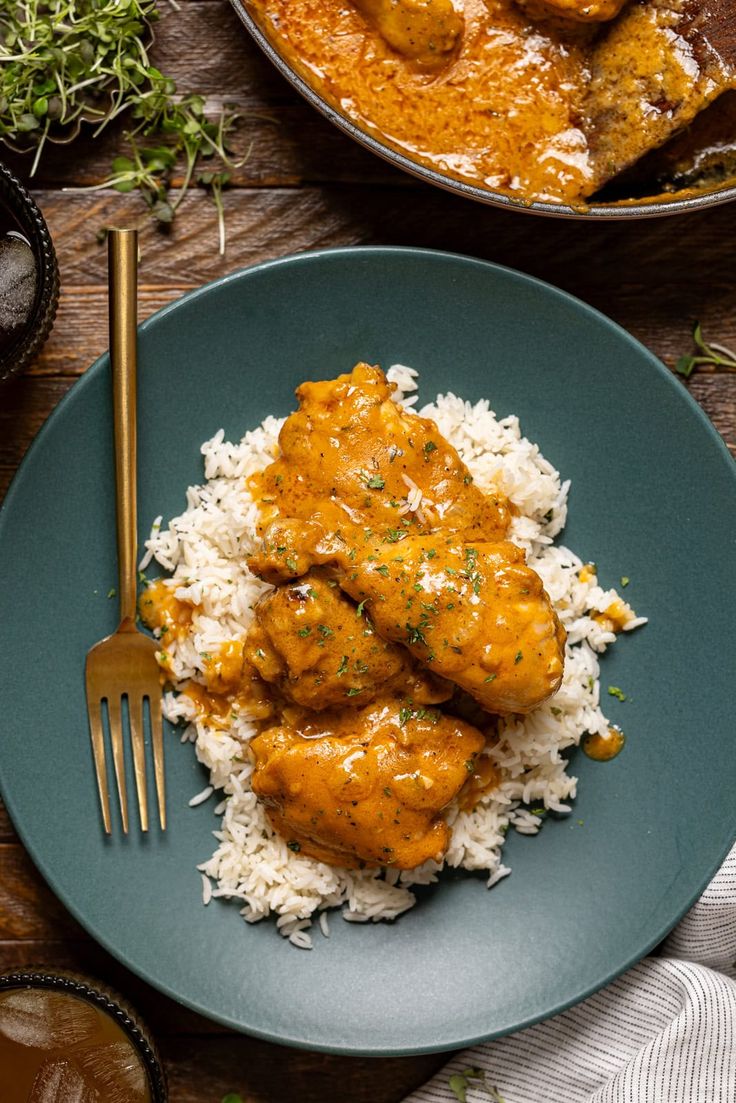 a blue plate topped with rice and meat covered in gravy next to a fork