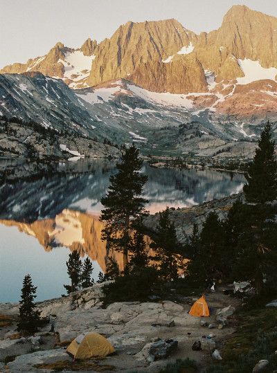 a tent pitched up on the side of a mountain next to a lake with mountains in the background