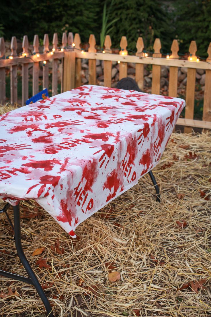 a red and white table covered in blood sitting on top of hay next to a fence