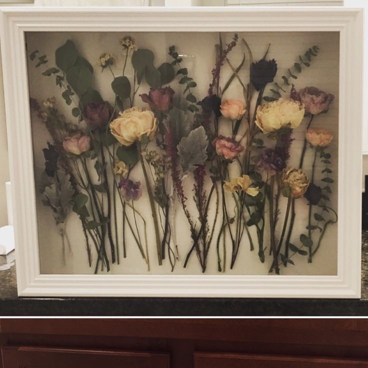 an arrangement of flowers is displayed in a white frame on a counter top with dark wood drawers