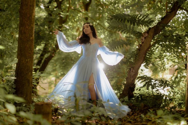 a woman in a blue dress is standing among the trees and leaves with her arms outstretched