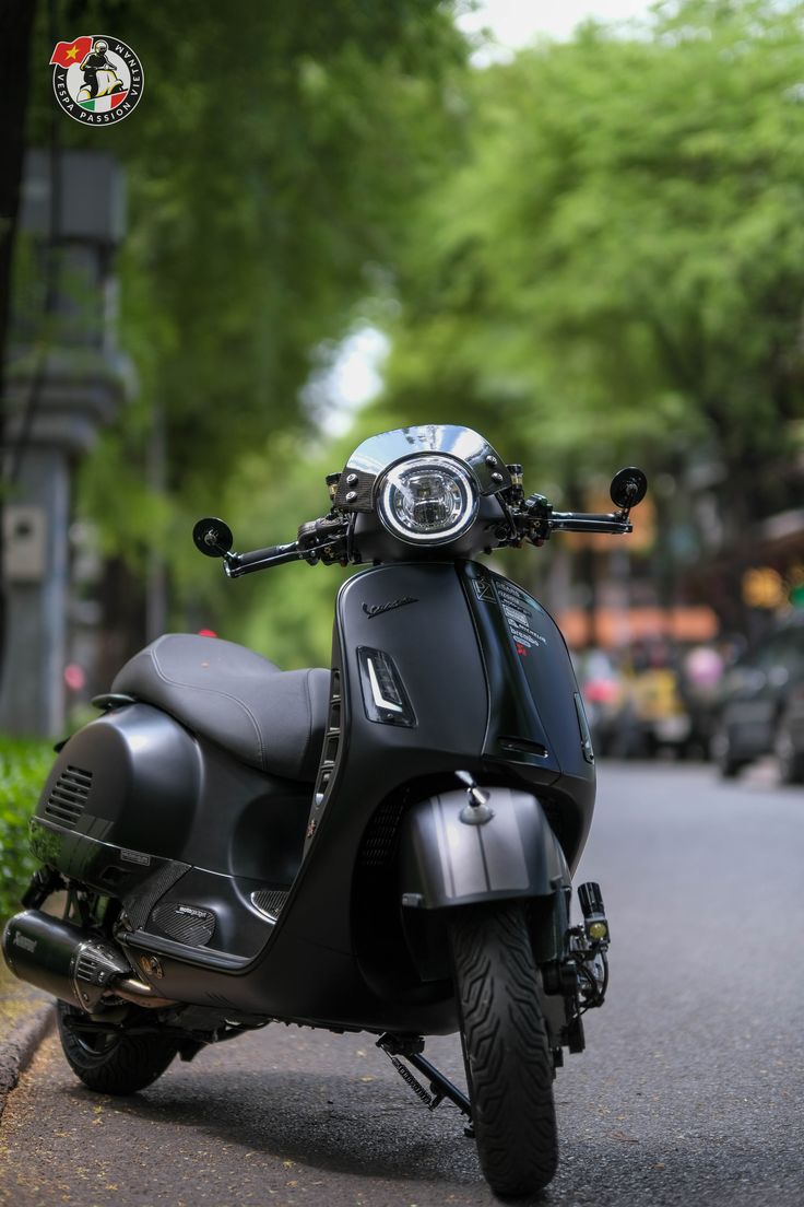 a black scooter parked on the side of a road next to a tree