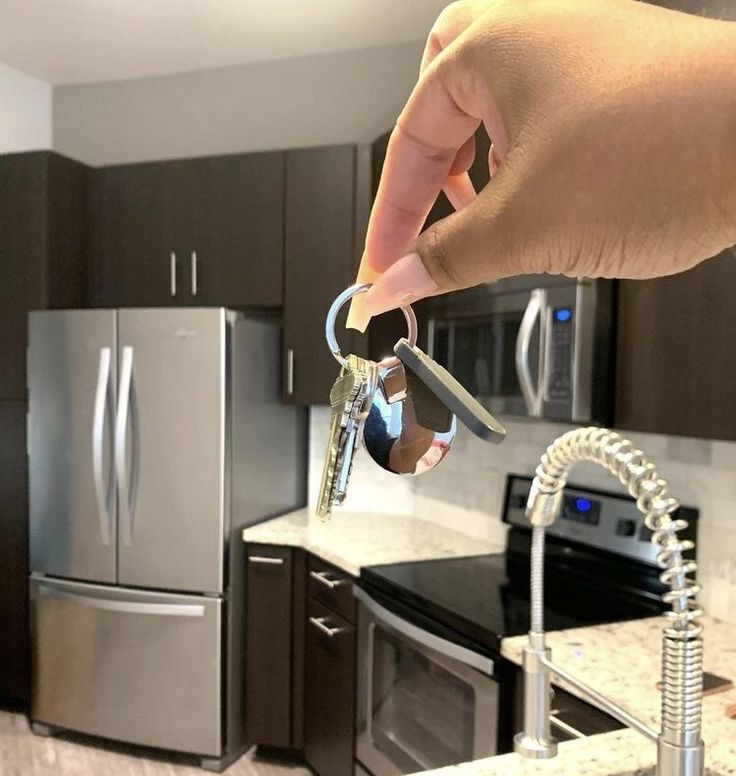 a person holding two keys in front of a kitchen with stainless steel appliances and granite counter tops