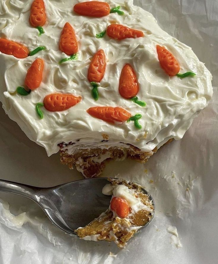 a carrot cake with frosting on top and a spoon in the foreground next to it