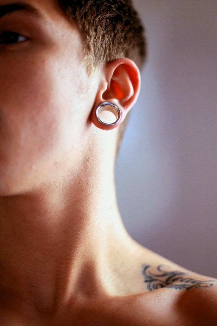 a close up of a person with tattoos on their chest and behind them is an ear ring