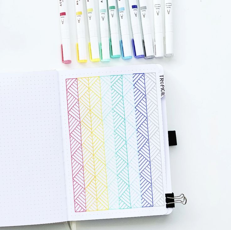 an open notebook with markers and pens next to it on top of a white surface