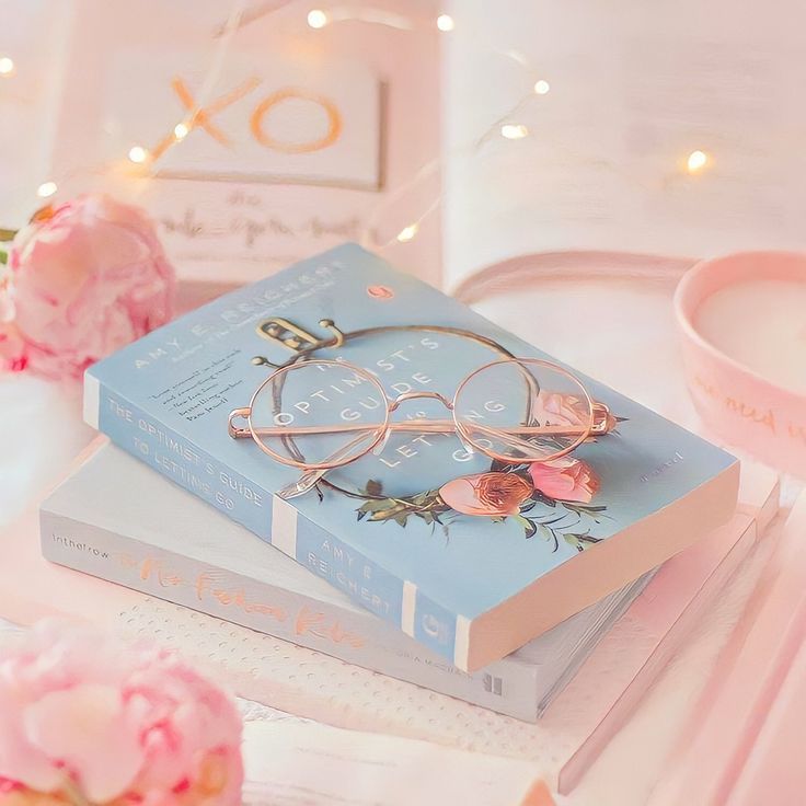 a stack of books sitting on top of a table next to pink flowers and glasses