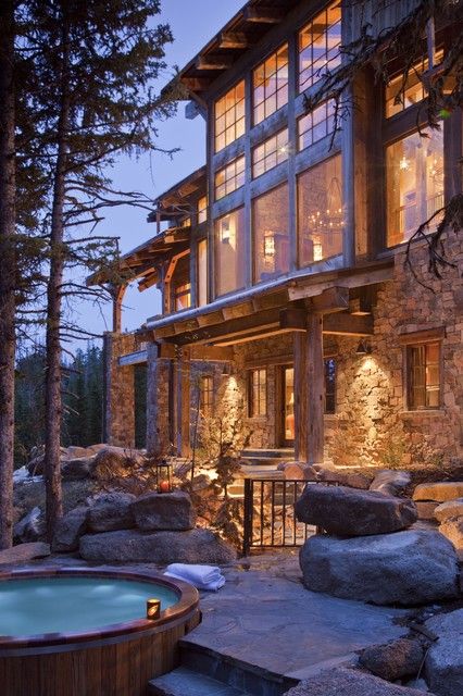 an outdoor hot tub in front of a house with stone walls and windows at night