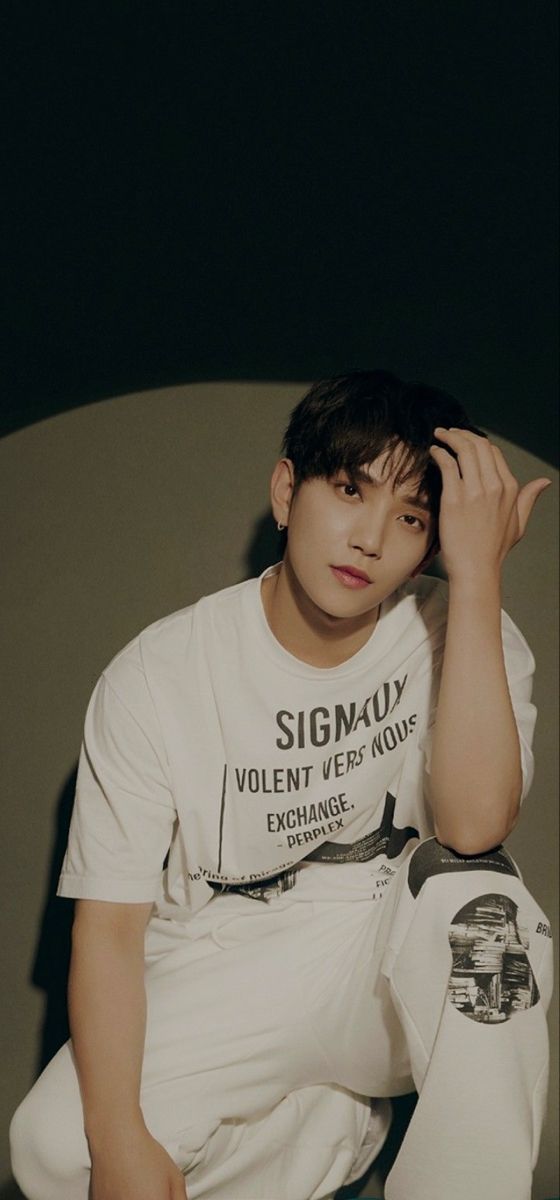 a young man sitting on top of a bed wearing a white t - shirt and pants