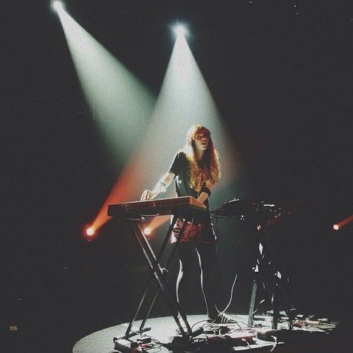 a woman standing in front of a keyboard on top of a stage with spotlights