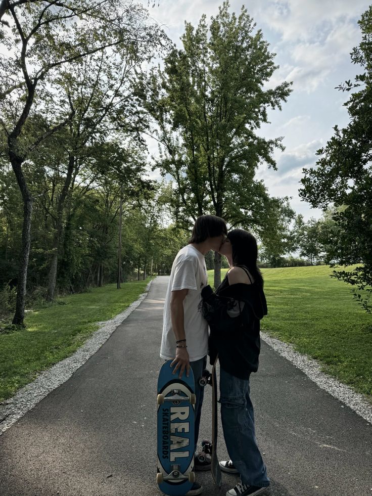 two people standing next to each other on a road with a skateboard in front of them