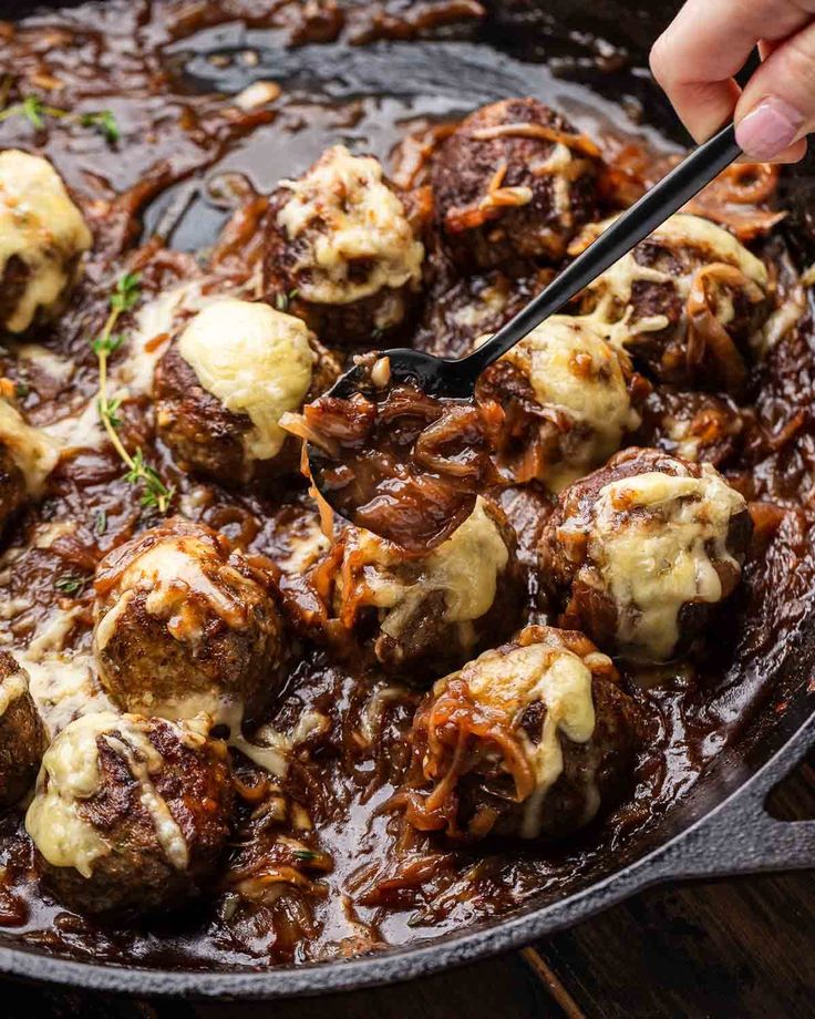 someone is spooning some meatballs with gravy in a cast iron skillet