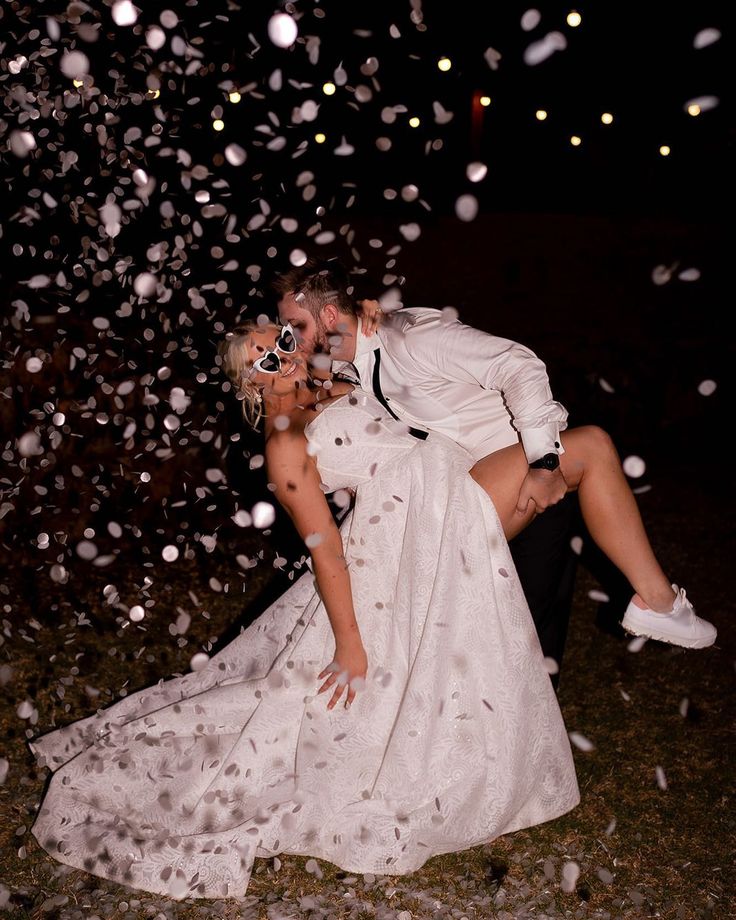 a bride and groom kissing in front of confetti falling from the sky at night