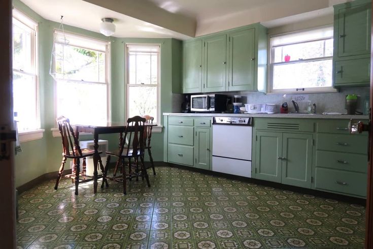 a kitchen with green cabinets and tile flooring in the center, along with two windows