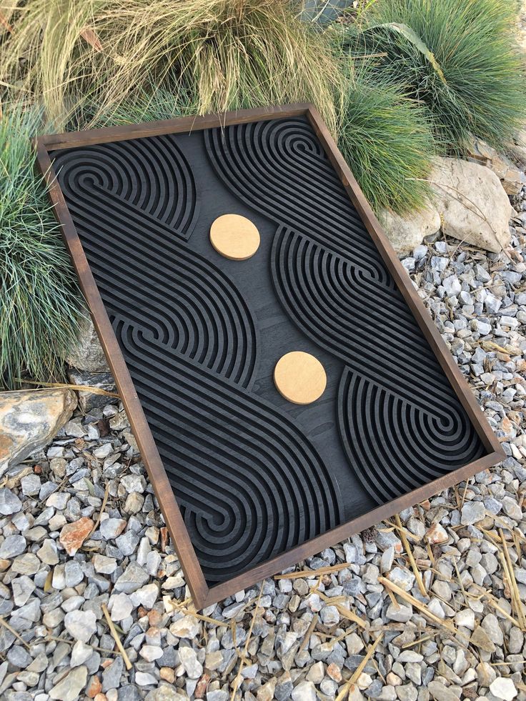 a black and brown decorative object sitting on top of some rocks next to plants with yellow circles in the center