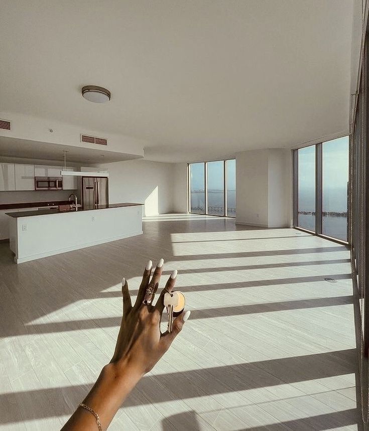 a person's hand reaching up towards the sky in an empty room with large windows