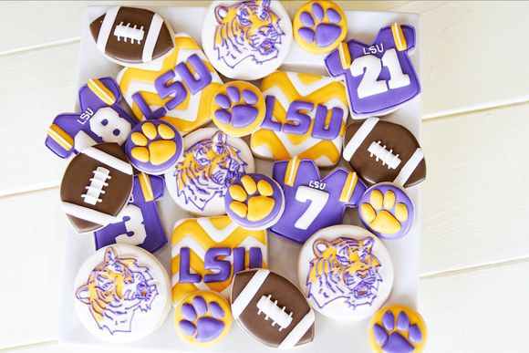 decorated cookies with footballs and tigers are on a white tray next to a wooden wall