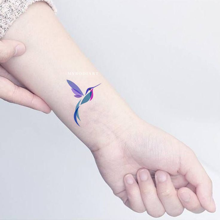 a small hummingbird tattoo on the left inner arm and wrist, with blue wings