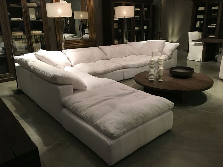 a large white sectional couch sitting in a living room next to a table with two lamps on it