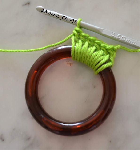 an orange ring with green yarn and a crochet hook next to it on a marble surface