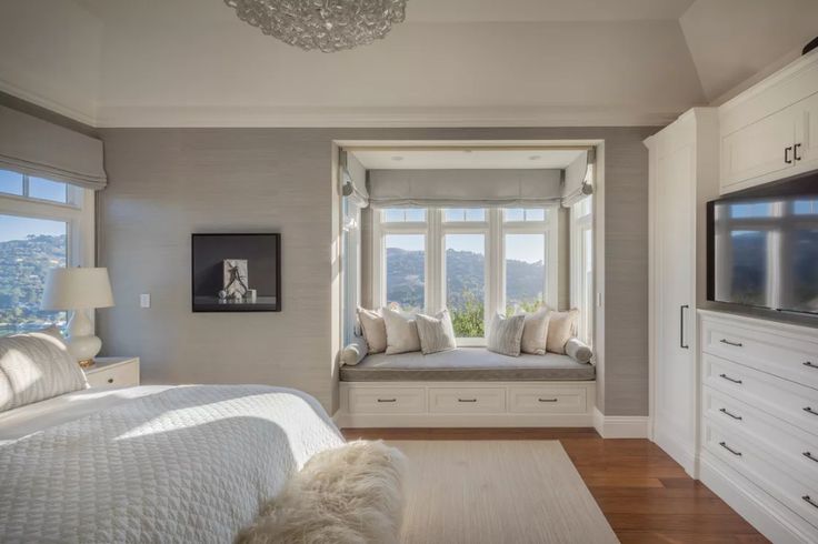 a bedroom with a large window seat next to a tv on top of a dresser