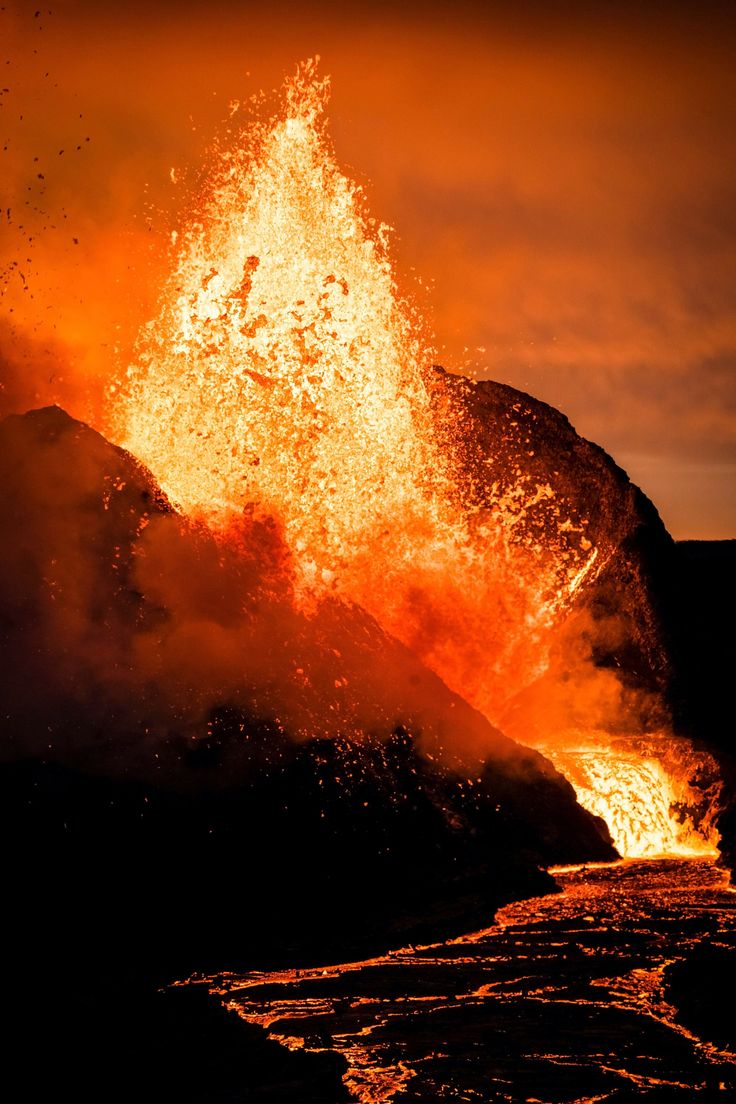 an orange and black volcano spewing out lava into the air at night time