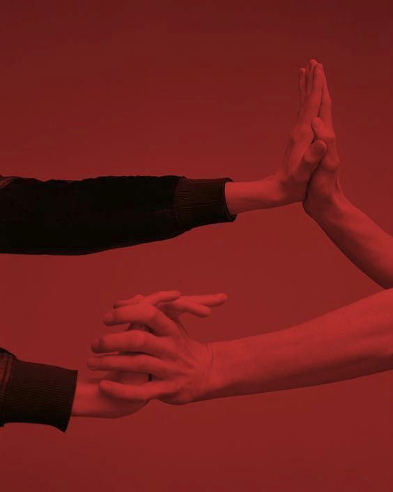 three people are holding their hands together in the air with red lighting behind them and one person is reaching out for something