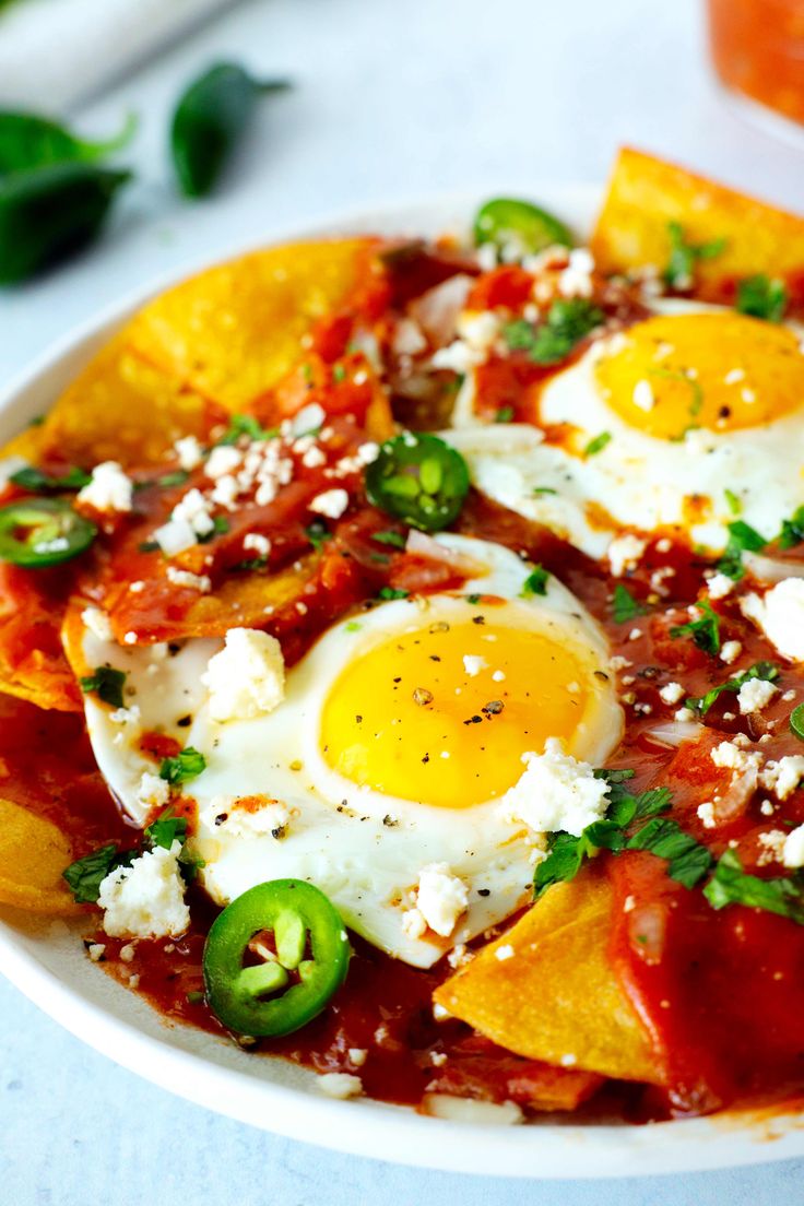 two fried eggs are on top of nachos with peppers and cheese in a bowl