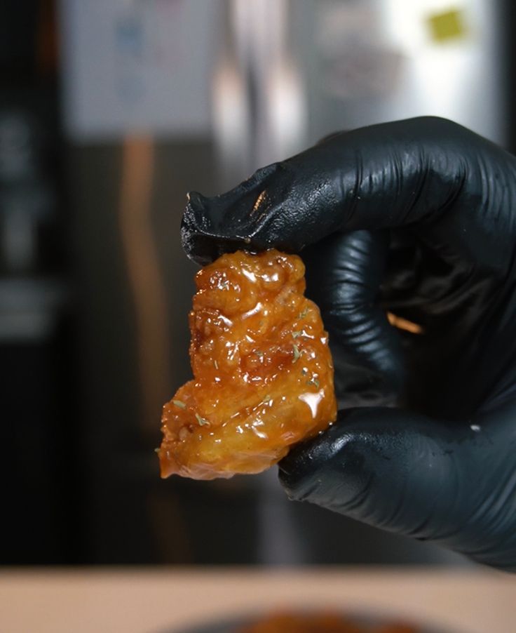 a person in black gloves holding up a piece of food that is covered in jelly